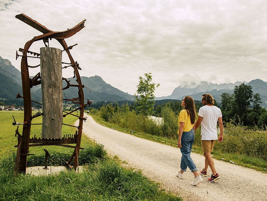 Wanderndes Pärchen betrachtet Skulptur am Wegesrand